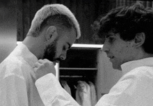 a man with a beard adjusts another man 's shirt collar