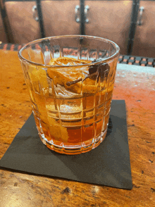 a glass of whiskey sits on a black napkin on a wooden bar