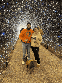 a man wearing an utre sweatshirt stands next to a woman holding a dog