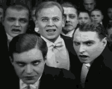 a black and white photo of a group of men in tuxedos and bow ties looking at the camera .