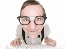 a nerd with glasses and a bandage on his nose is typing on a computer keyboard .