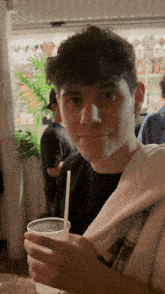 a young man with curly hair is holding a cup with a straw in it