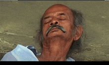 a man with a mustache is sleeping on the ground with his eyes closed .