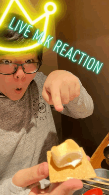 a person wearing glasses and a crown holds a s'more with the words live mk reaction written on it