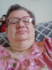 a woman wearing glasses and a pink floral shirt is laying on a couch