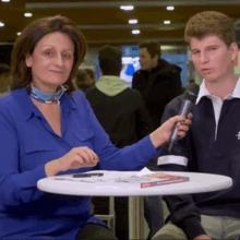 a woman in a blue shirt is holding a microphone next to a young man