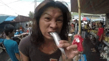 a woman is eating a fish in a market with a crowd behind her .