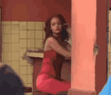 a woman in a red dress is sitting on a stool in front of a wall .