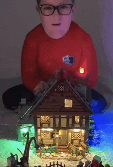 a boy wearing glasses is playing with a house made of lego