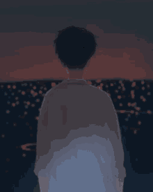 a man in a white shirt looks out over a body of water at night