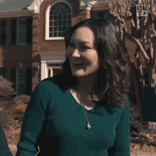 a woman in a green sweater is standing in front of a brick house with a sign that says be