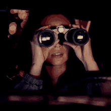 a woman is looking through binoculars at a window at night .