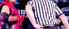 a referee in a striped shirt is standing next to a wrestler in a pink shirt .