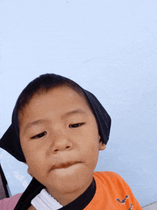 a young boy wearing an orange shirt with bats on it looks at the camera