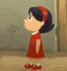 a little girl in a red dress and red shoes is standing next to a door .