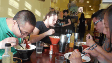 a group of people are sitting at a table eating food with chopsticks