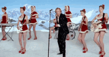 a man singing into a microphone surrounded by women dressed as santa claus