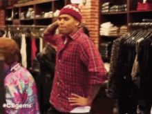 a man in a plaid shirt is standing in a clothing store with his hand on his hip