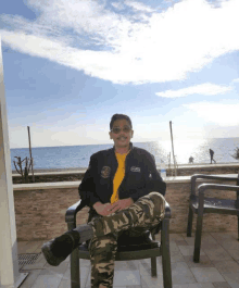 a man sitting in a chair with his legs crossed wearing a black jacket that says army