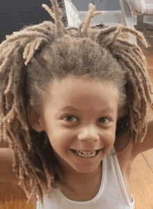 a young boy with dreadlocks and a white tank top is smiling .