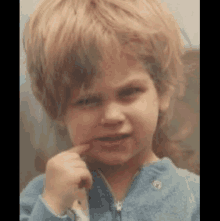 a young boy with blonde hair is making a funny face and holding his finger to his mouth .