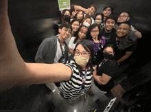 a group of people are posing for a picture in front of a sign that says " please wear a face mask "