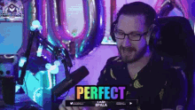 a man wearing glasses is sitting in front of a microphone with a rainbow sign that says perfect .