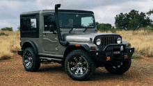 a mahindra jeep is parked in the dirt in a field