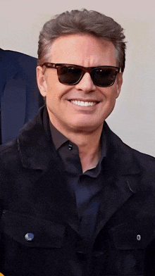 a man wearing sunglasses and a jacket smiles for the camera