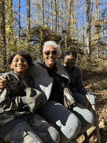 three people sitting on a bench in the woods with one wearing a nike jacket