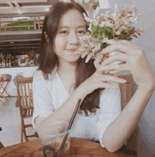 a woman is sitting at a table holding a bouquet of flowers and drinking a drink .