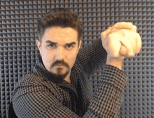 a man in a plaid shirt holds his fist up in front of a pyramid patterned wall