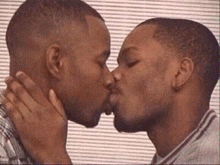 two men are kissing each other on the cheek in front of a striped wall .