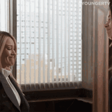 two women are talking in front of a window with youngertv written on the bottom right corner