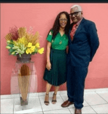 a man and a woman are standing next to a vase of flowers .