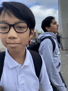 a boy wearing glasses stands next to another boy wearing a sweatshirt that says ' rs ' on it