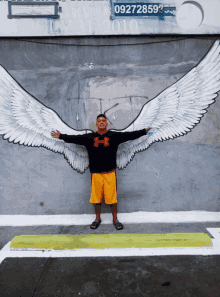 a man wearing a black under armour sweatshirt stands in front of a painting of angel wings