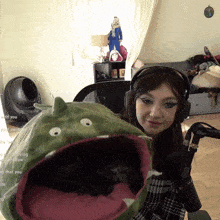 a woman wearing headphones sits in front of a stuffed animal that looks like a dinosaur with its mouth open