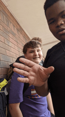 a boy in a purple shirt holds out his hand towards the camera