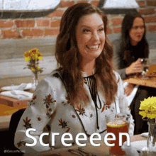 a woman is smiling while sitting at a table with a glass of beer and the words screeeen above her