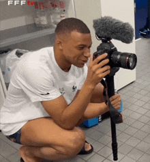 a man is kneeling down while holding a camera in a room .