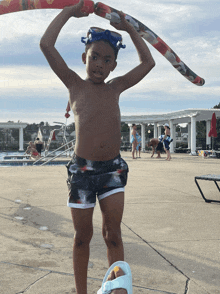 a young boy holds a hula hoop over his head in front of a swimming pool