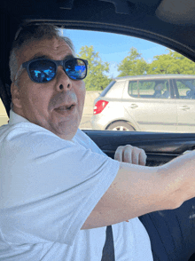 a man wearing sunglasses is driving a car and making a funny face