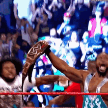 a man in a wrestling ring holds up a championship belt in front of a crowd that says the next round