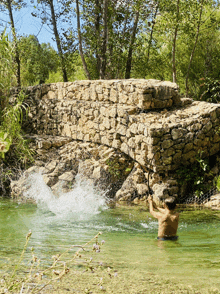 a shirtless man is fishing in a river with a stone wall in the background