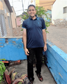 a man wearing a blue polo shirt and black pants stands in front of a blue wall