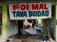 a man is sitting under a sign that says foi mal tava doidoo