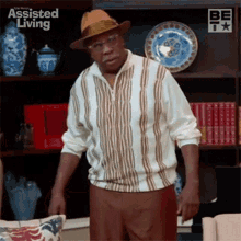 an older man wearing a hat and glasses is standing in front of a bookshelf in a living room .