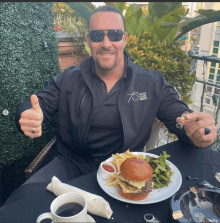 a man is sitting at a table with a plate of food and a jacket that says 75 on it