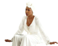 a woman in a white dress with a cross necklace sits on the floor